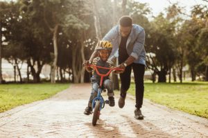 father teaching child to ride bike in park