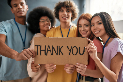 group of young adults hold thank you for giving back sign
