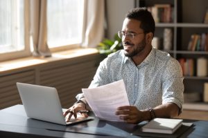 man working on tax forms, using computer and holding form in hand